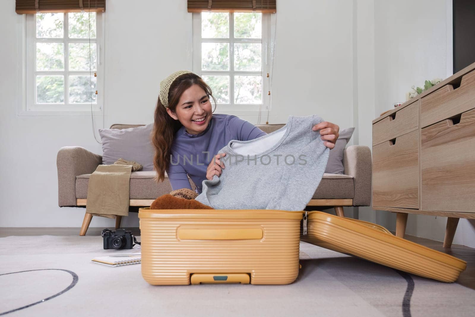 Attractive Asian woman packs her suitcase, packing her belongings, clothes and travel documents before going on vacation. Lifestyle concept.
