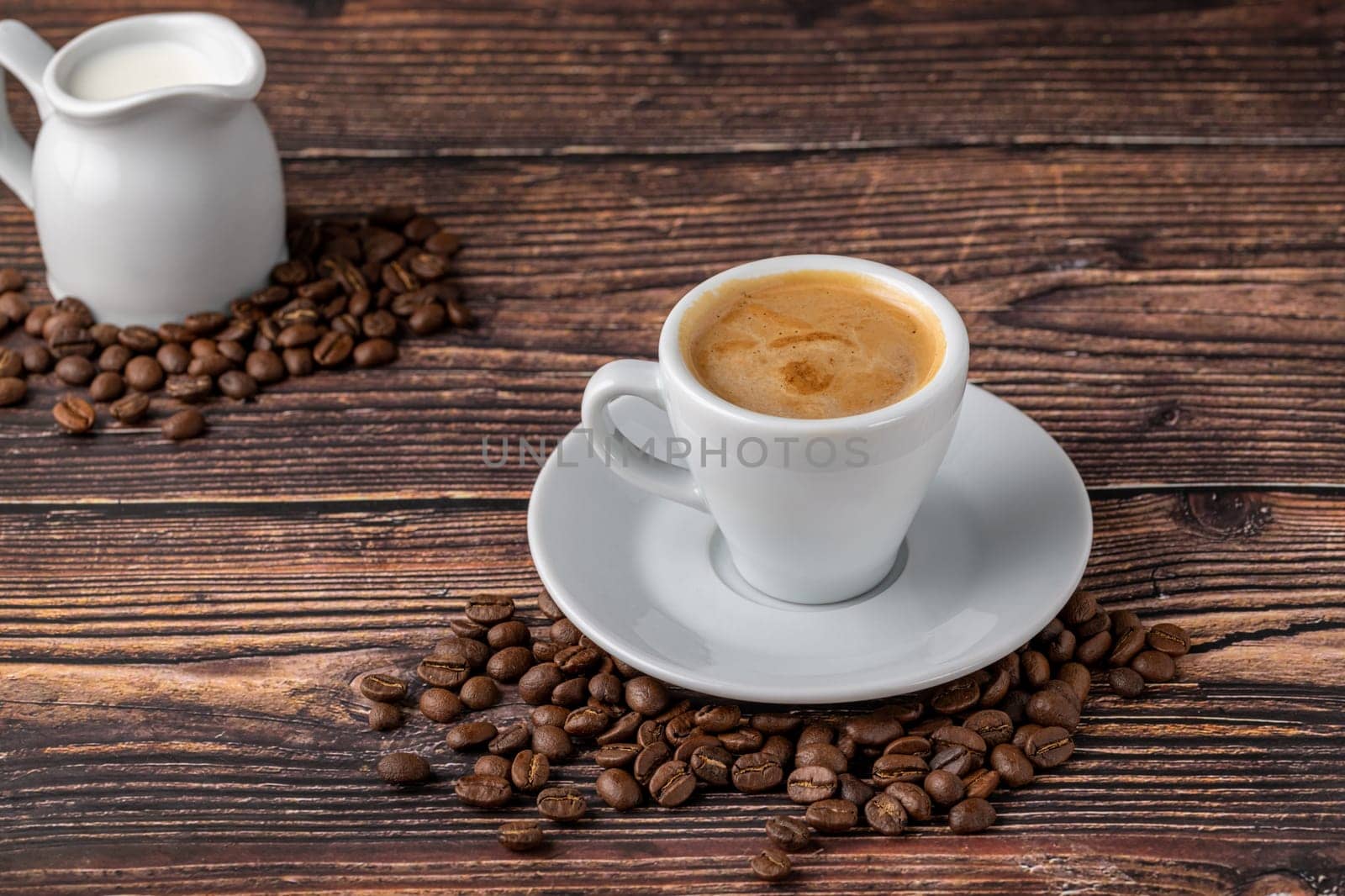 Espresso macchiato in white porcelain cup with milk and coffee beans on wooden table