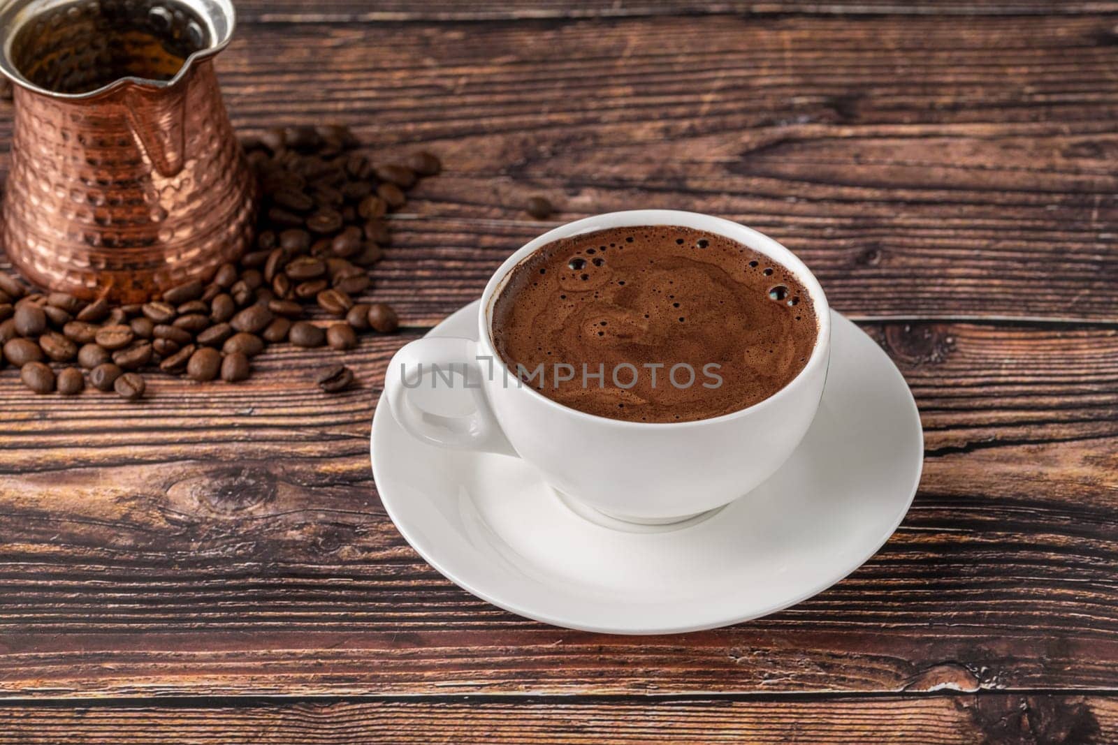 Double Turkish coffee in a white porcelain cup with a decorative coffee pot on a wooden table by Sonat