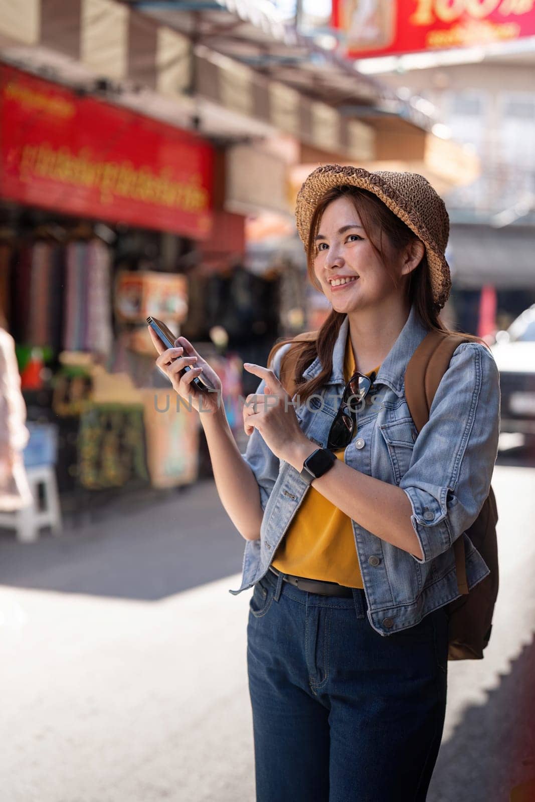 Happy young Asian tourist woman using smartphone on street with market background, Female traveller enjoy shopping market during holidays by nateemee