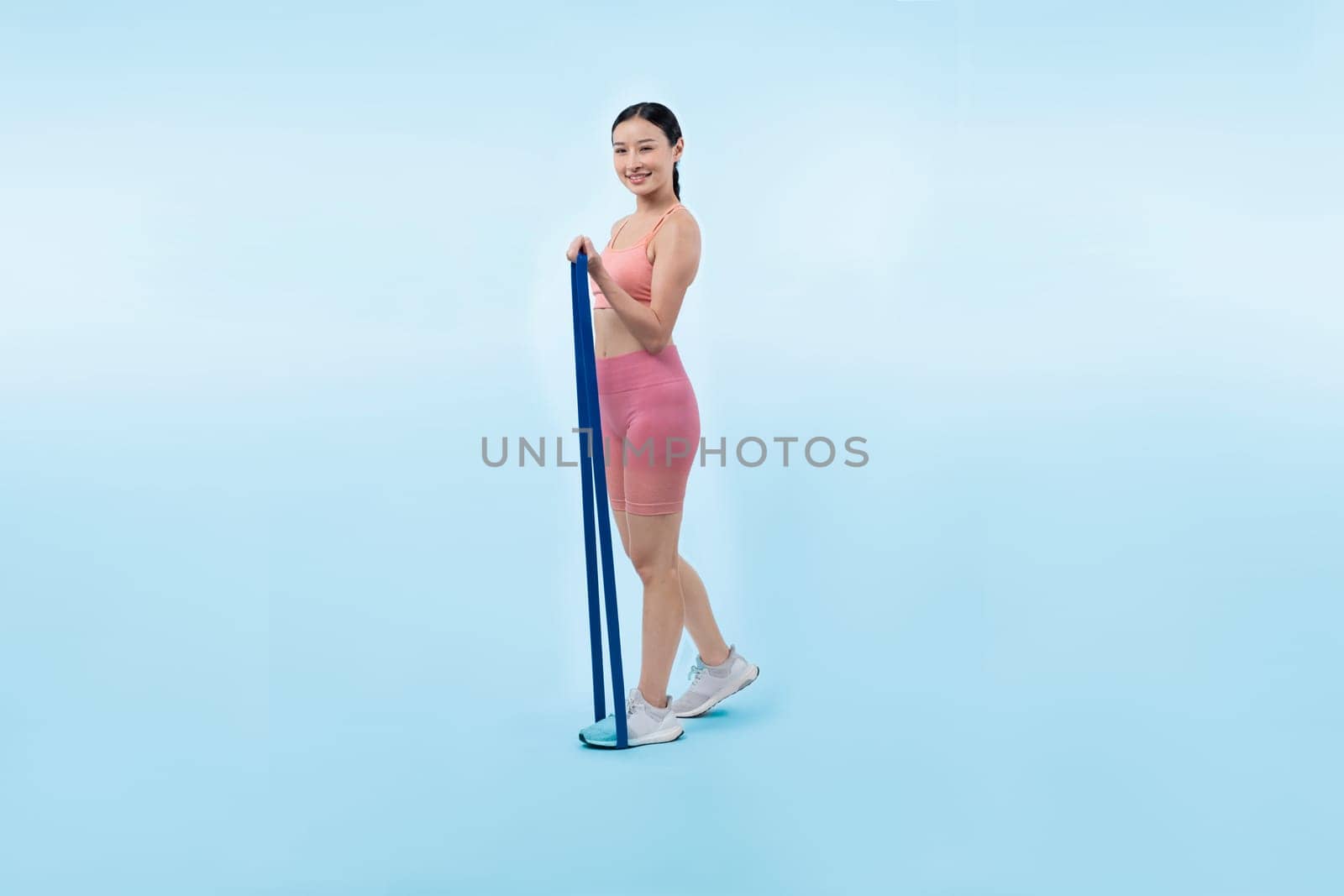 Vigorous energetic woman in sportswear portrait stretching resistance sport band. Young athletic asian woman strength and endurance training session workout routine concept on isolated background.