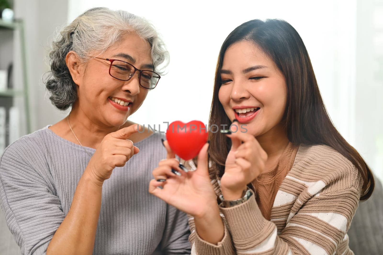 Smiling gray haired mature woman and daughter holding red heart. Health care, insurance and world heart day concept.