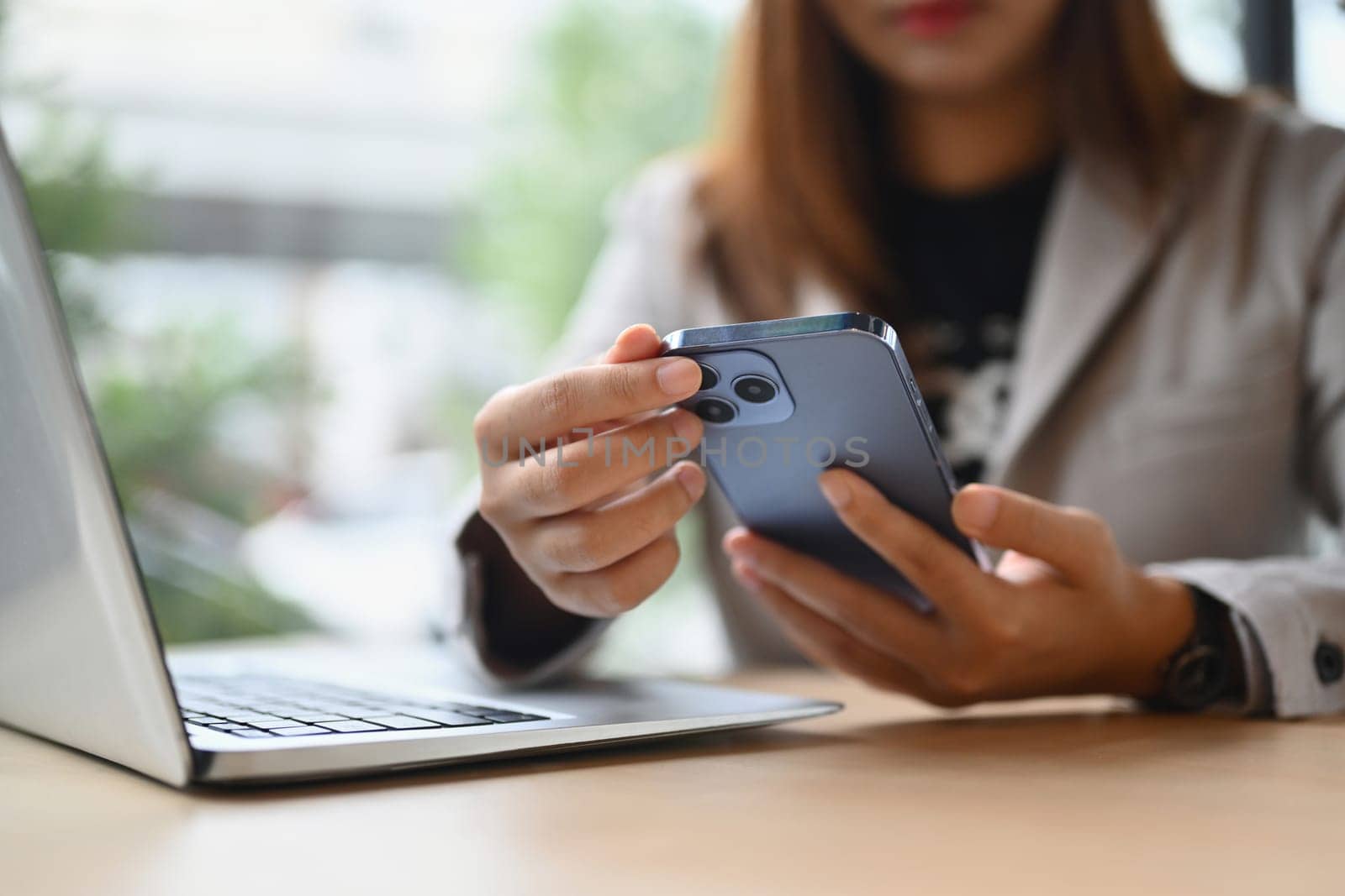 Modern businesswoman sitting front of laptop at coffee shop and using mobile phone.