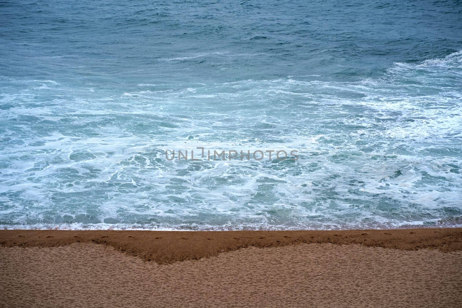 Top view over the sea beach. Beautiful sea waves. Sandy beach and stunning sea. Summer sunset seascape. Water texture. Human footprints on wet sand.