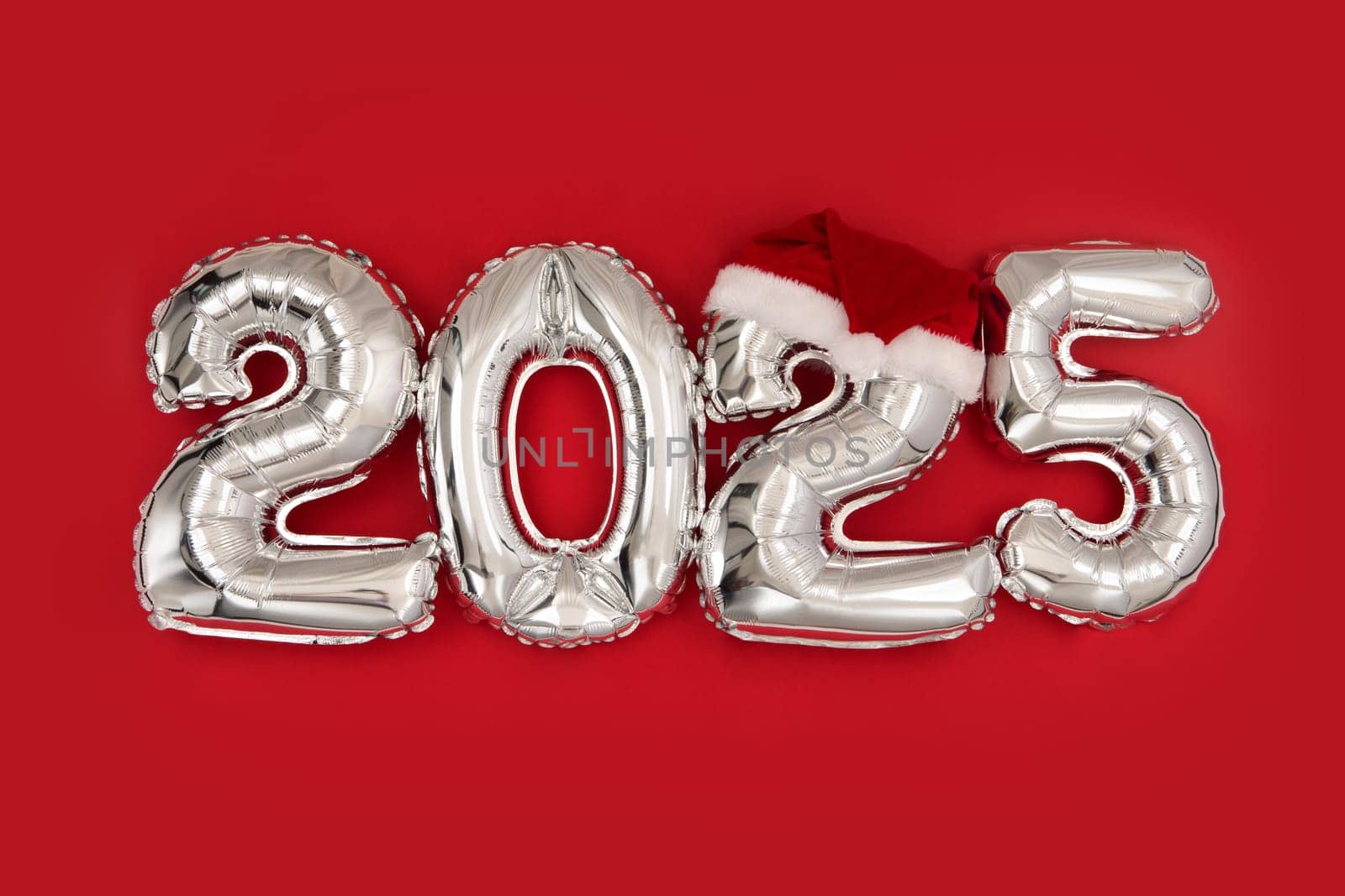 2025 inflatable balloons on red background with Santa hat. Happy New year twenty twenty five celebration. Silver foil balloons numeral 2025. Postcards and posters Copy space