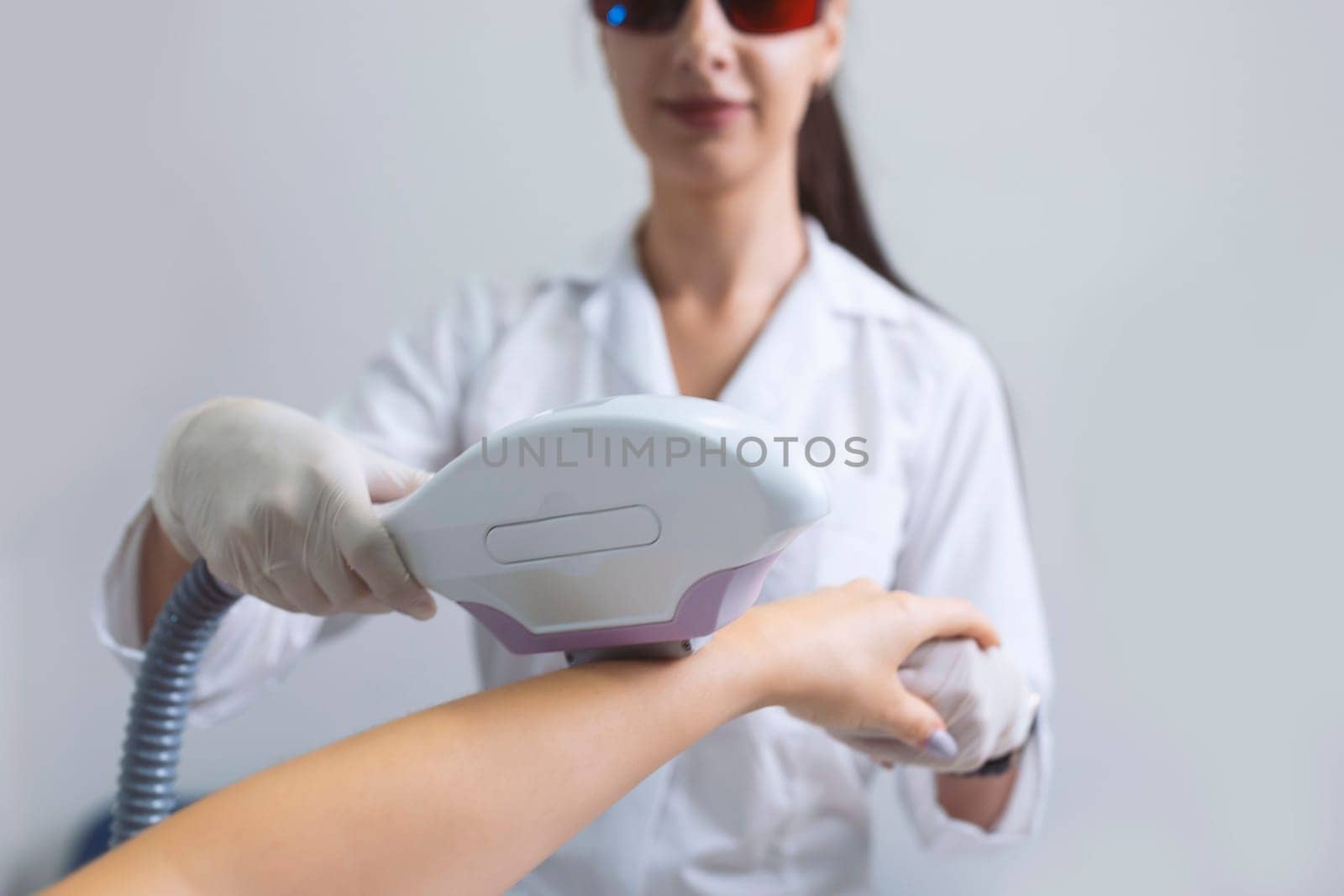 Woman in a beauty salon removes hair from her arm with laser epilation