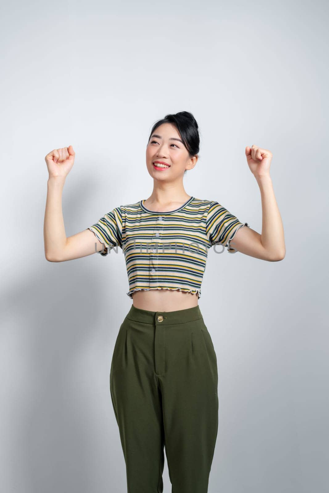 Beautiful Asian woman raises arms and fists clenched with celebrating victory expressing success. by makidotvn