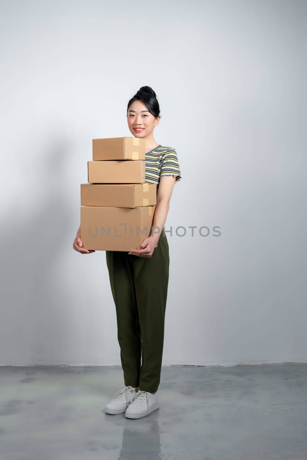 Happy Asian girl holding package parcel boxs isolated on gray background. by makidotvn