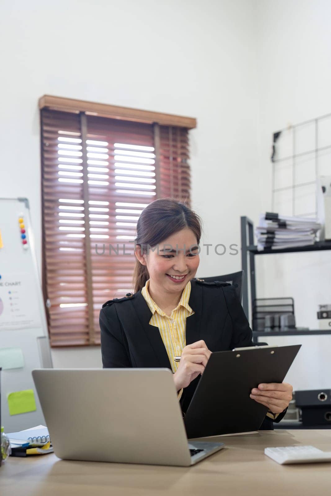 Young asian businesswoman sitting at desk with data and graph by using calculator finance accounting analyze, plan, and strategy about business improvement.