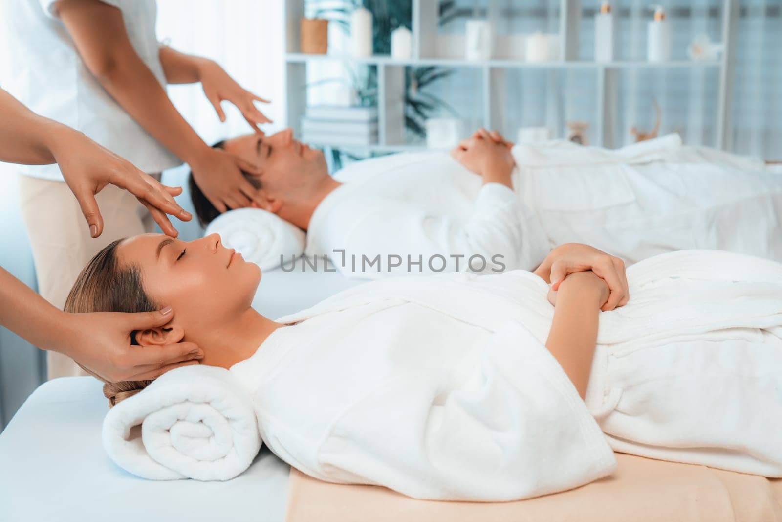 Caucasian couple enjoying relaxing anti-stress head massage and pampering facial beauty skin recreation leisure in dayspa modern light ambient at luxury resort or hotel spa salon. Quiescent