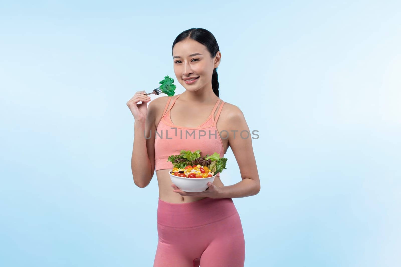 Young sporty Asian woman in sportswear holding salad bowl fill with vibrant of fruit and vegetable. Natural youthful and fit body lifestyle with balance nutrition on isolated background. Vigorous