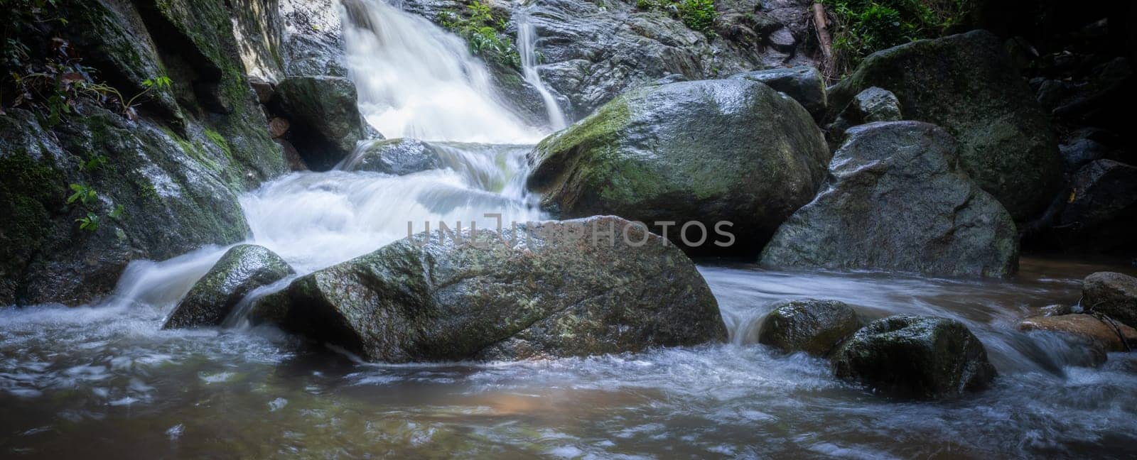 Waterfall is flowing in jungle. Waterfall in green forest. Mountain waterfall. Cascading stream in lush forest. Nature background. Rock or stone at waterfall. Water sustainability. Water conservation. by Fahroni