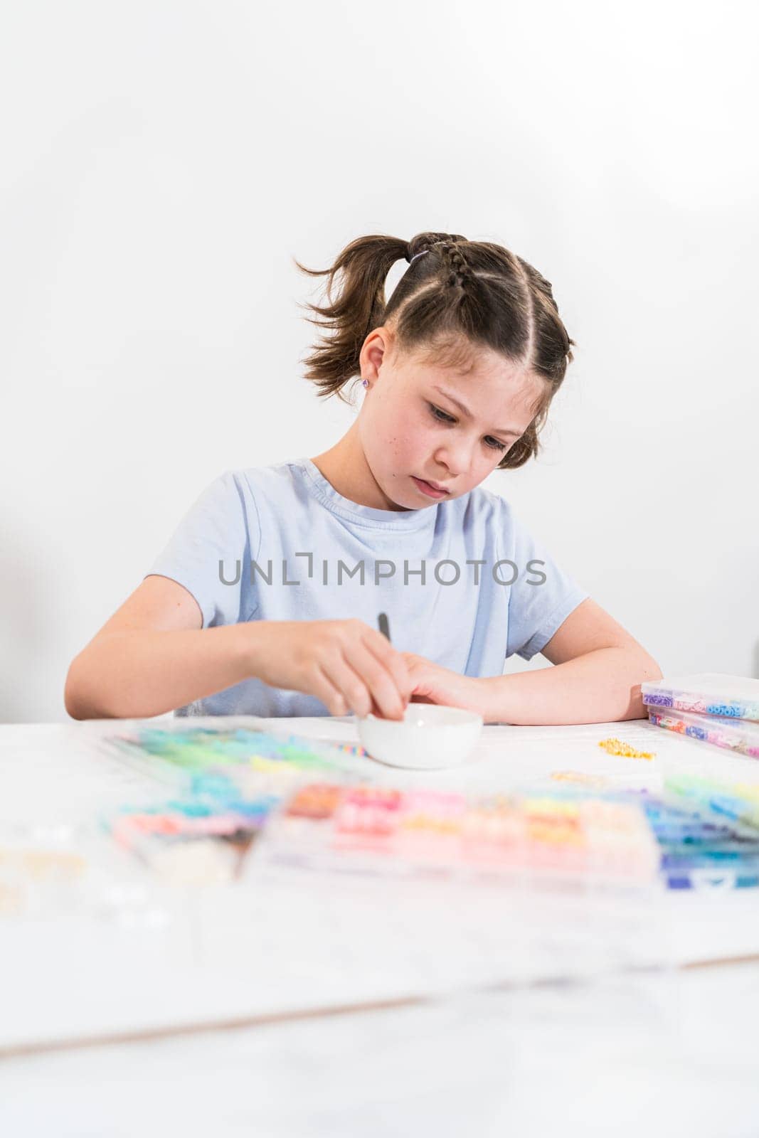 Little girl enjoys crafting colorful bracelets with vibrant clay beads set.