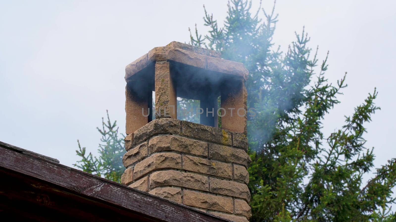A residential building in the suburbs on a cloudy day in a cold winter pollutes the air with thick dark smoke. Smog coming out of the chimney.