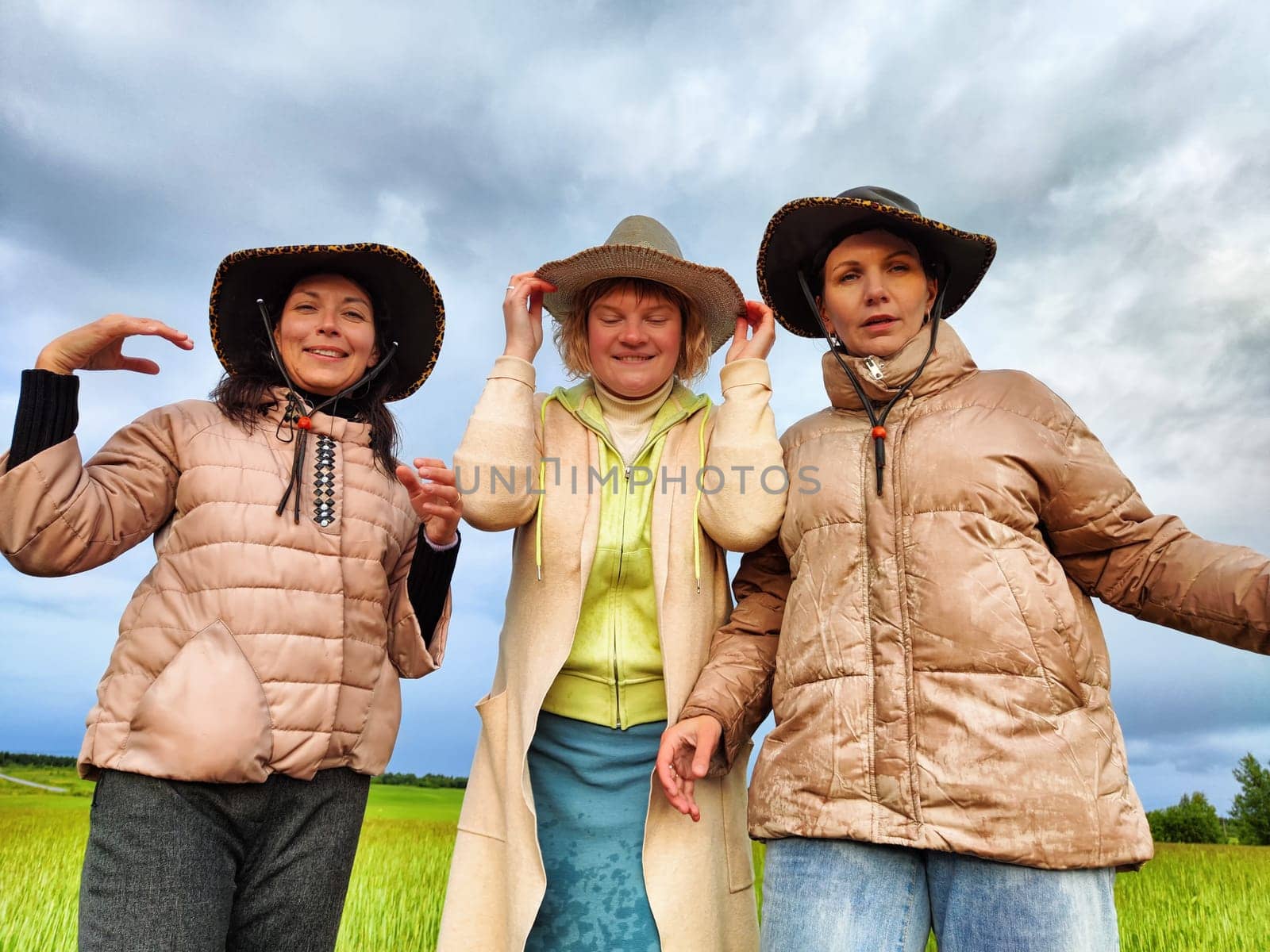 Adult girls looking like a cowboys in hats in a field and with a stormy sky with clouds posing in the rain. Women having fun outdoors on rural and rustic nature