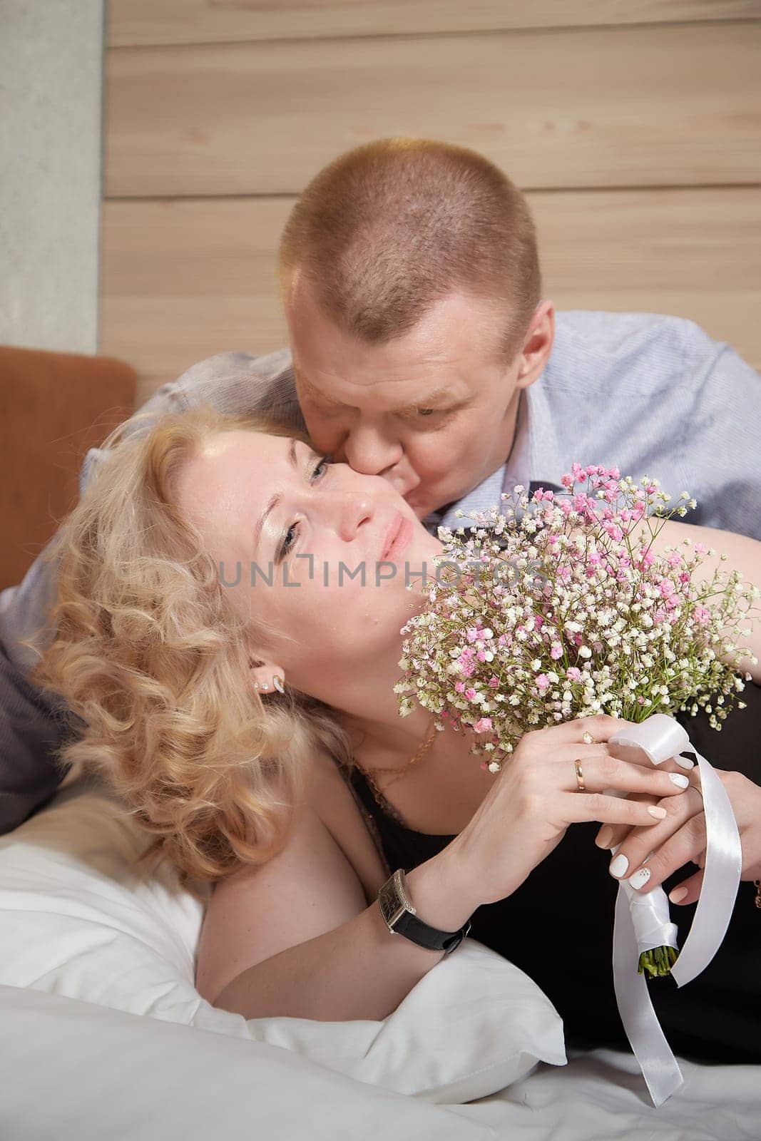 Loving enamored adult couple communicates, embraces, and has fun alone together on the bed in the bedroom or hotel room. The woman is wearing tank top and the man is shirtless