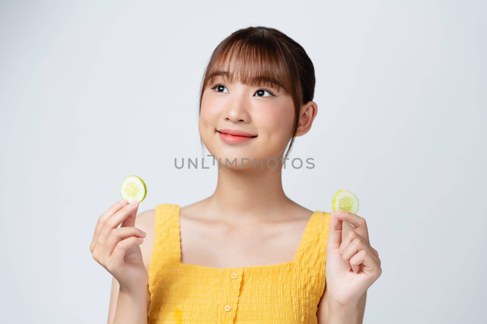 A picture of a face of a beautiful woman posing with a cucumber over white background