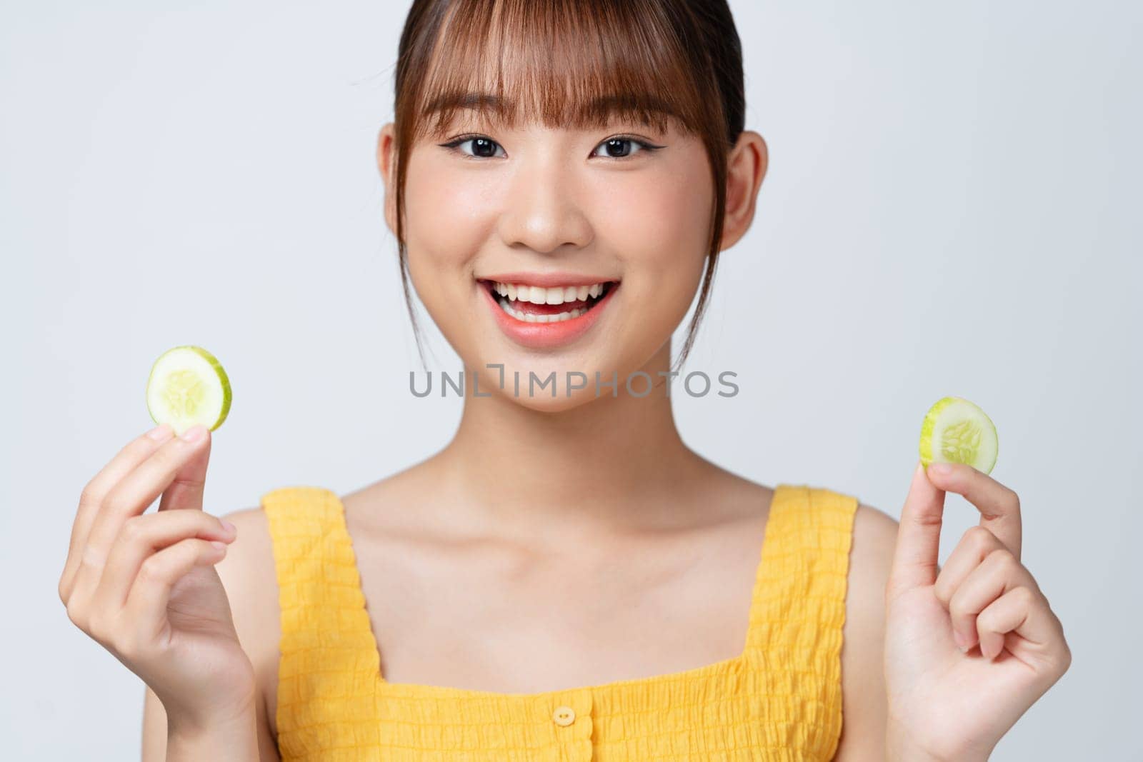 A gorgeous young woman holding cucumber slices while isolated on white background. by makidotvn