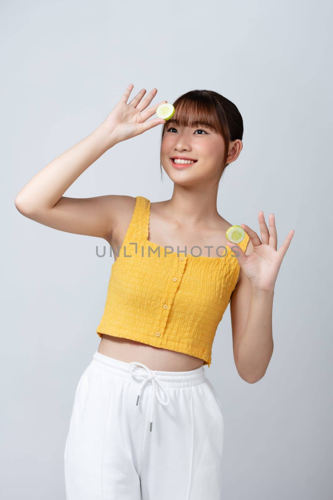 Young pretty woman holding slice of fresh cucumber over white background