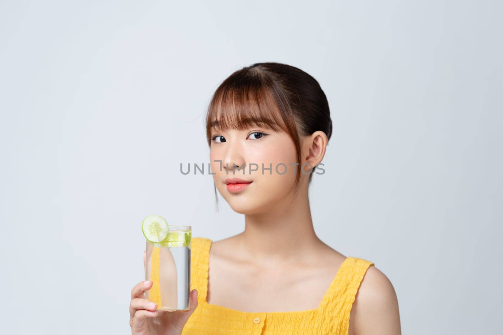 a beautiful young woman with a glass of water with cucumber slices isolated on white.