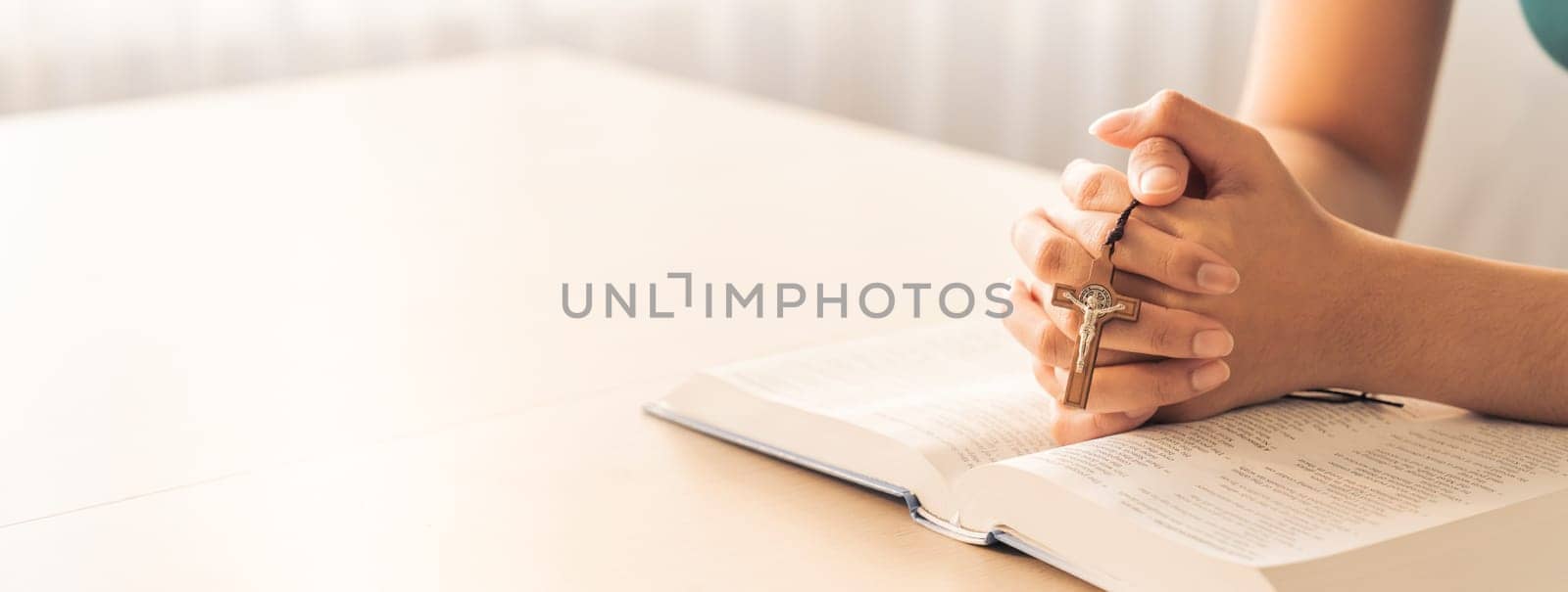 Cropped image of female reading a bible book while holding cross at wooden table with blurring background. Concept of hope, religion, faith, christianity and god blessing. Warm. Burgeoning.