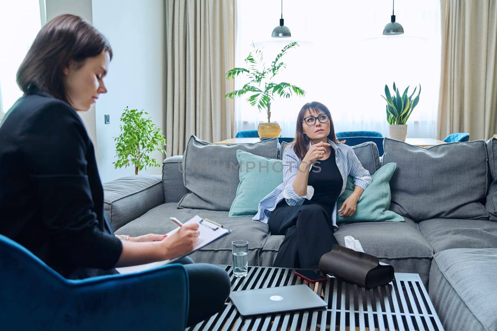 Middle aged woman on therapy session in psychologist's office. Therapist counselor social worker talking to 40s female patient taking notes. Psychology psychotherapy treatment support mental health