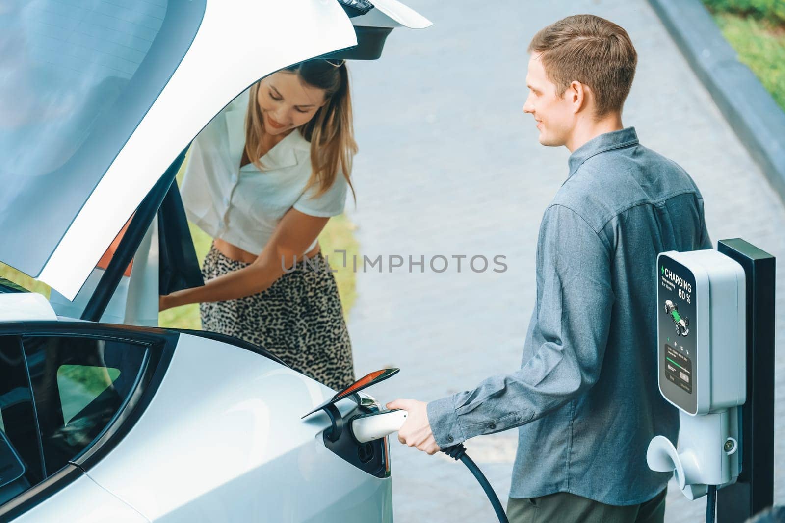 Young couple travel with EV electric car in green sustainable city innards by biancoblue