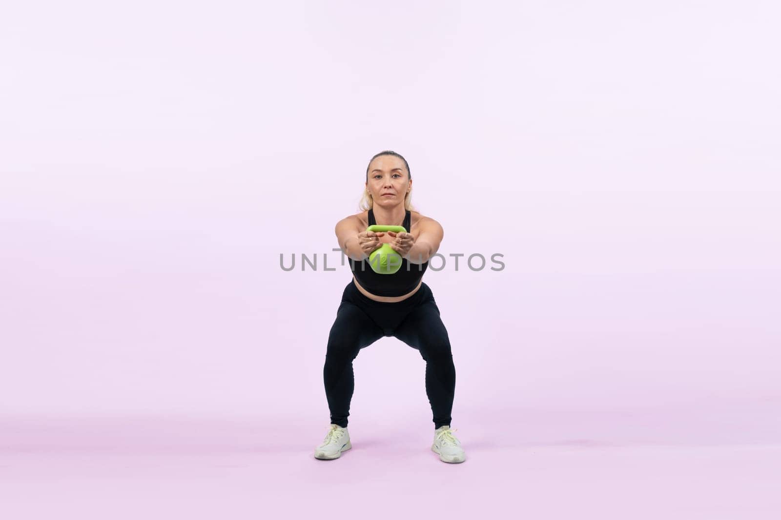 Full body length shot athletic and sporty senior woman doing squat with kettlebell for body workout on isolated background. Healthy active physique and body care lifestyle after retirement. Clout