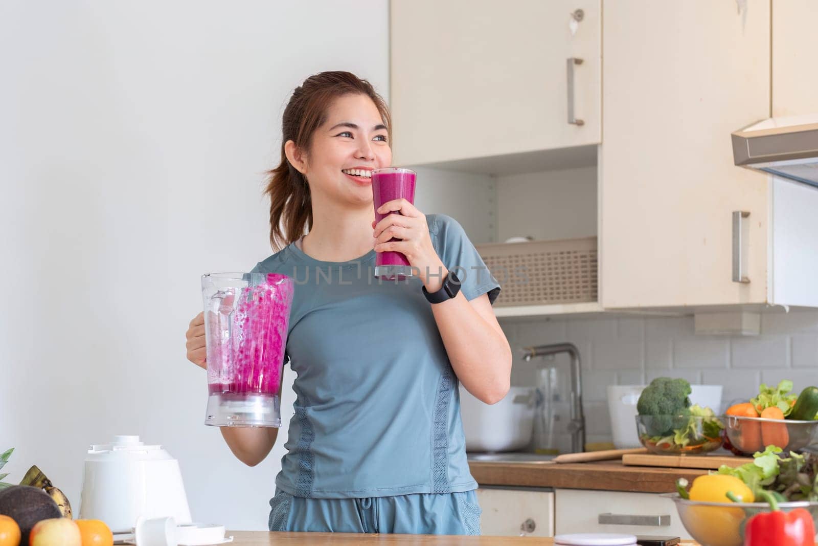 Young attractive Asian woman makes a fruit smoothie in the kitchen. Take care of your health by eating fruits and vegetables to add vitamins..