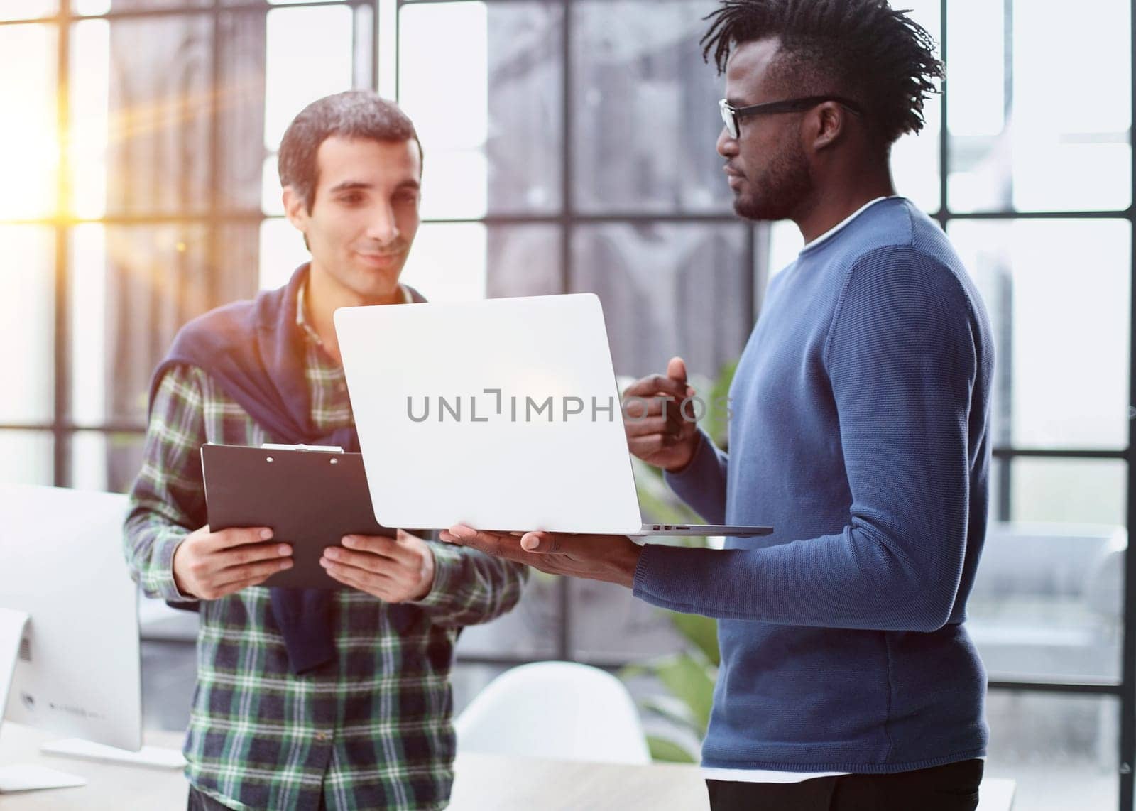 young business men standing together holding a laptop, discussing business by Prosto