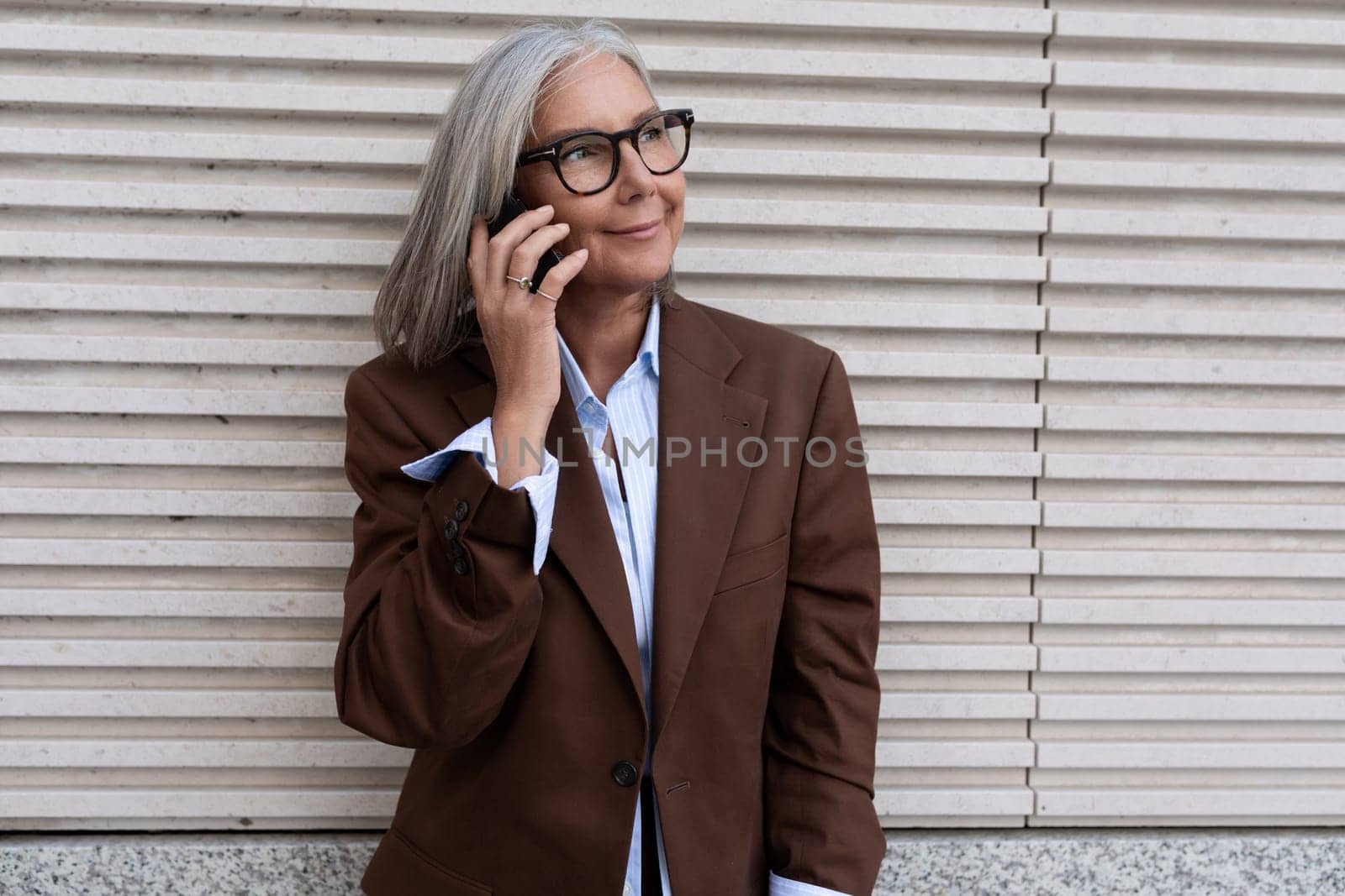 A 60 year old successful Caucasian business lady dressed in a brown stylish suit speaks on a smartphone. middle aged business concept.