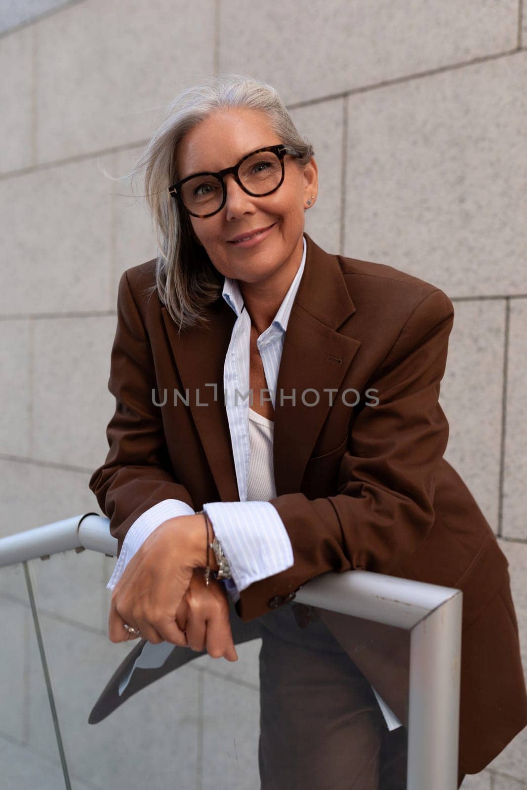 60 year old Caucasian business lady leader dressed in a brown stylish suit walks around the city.