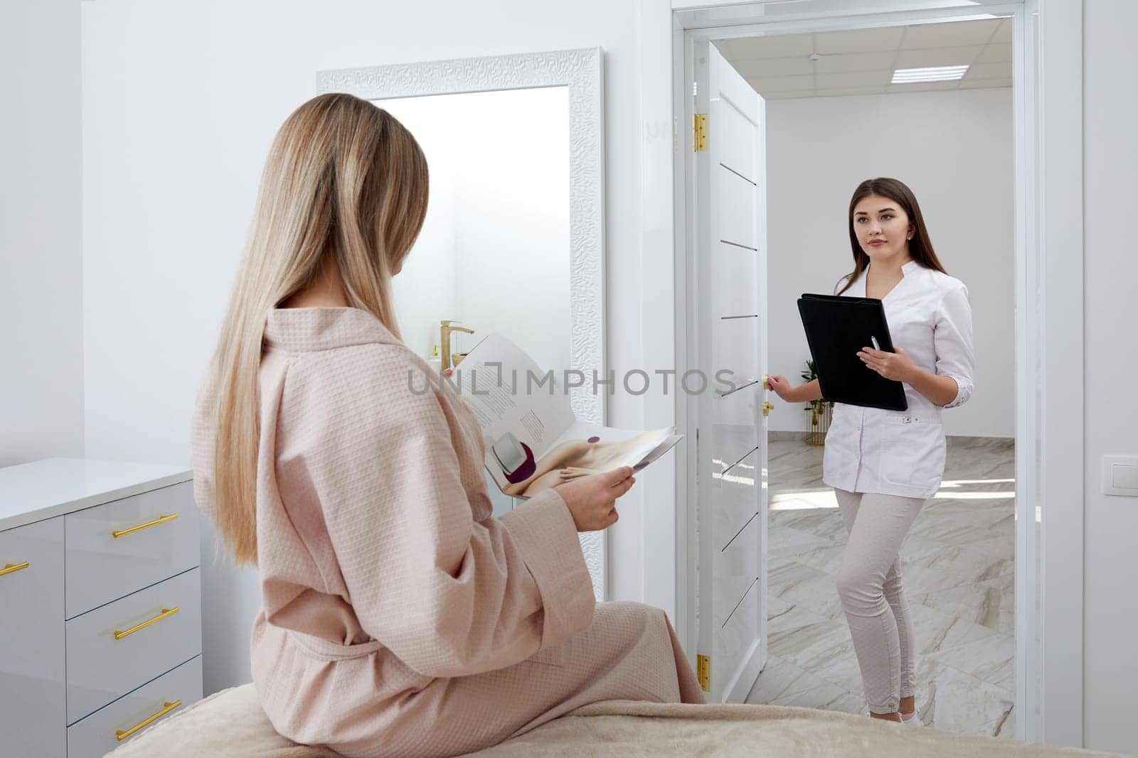 Young female cosmetologist confidently enters treatment room with waiting patient by Mariakray