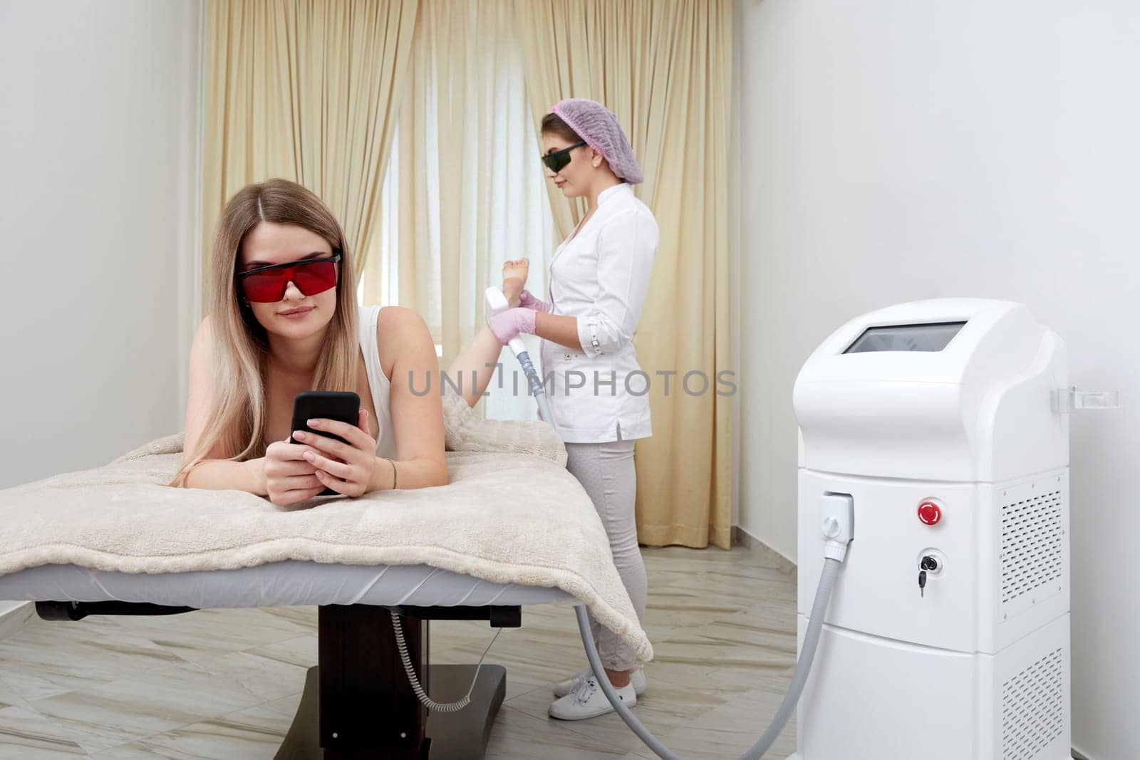 At beauty salon, woman relaxes during laser hair removal session on her legs by Mariakray