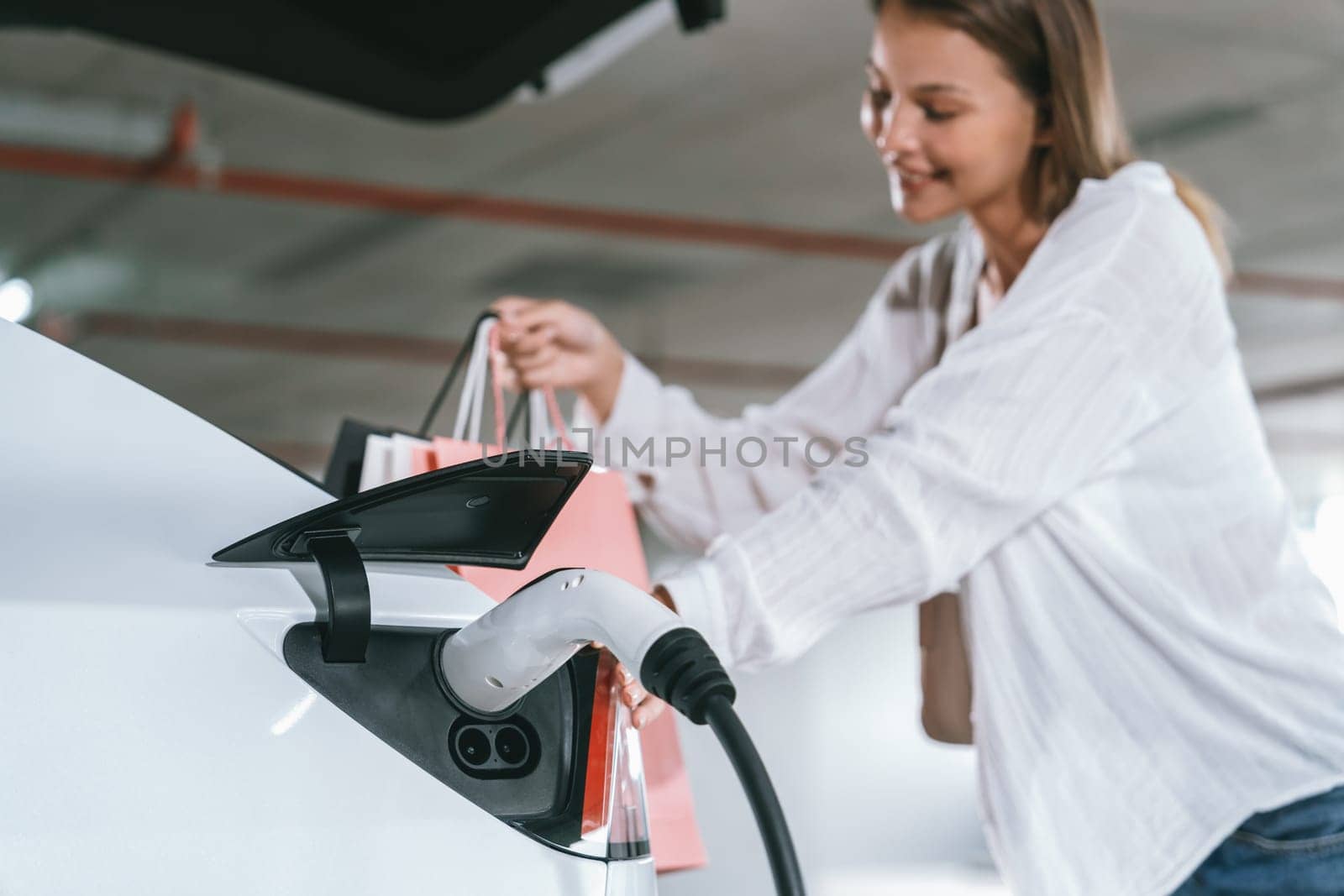 Young woman travel with EV electric car to shopping center parking lot innards by biancoblue