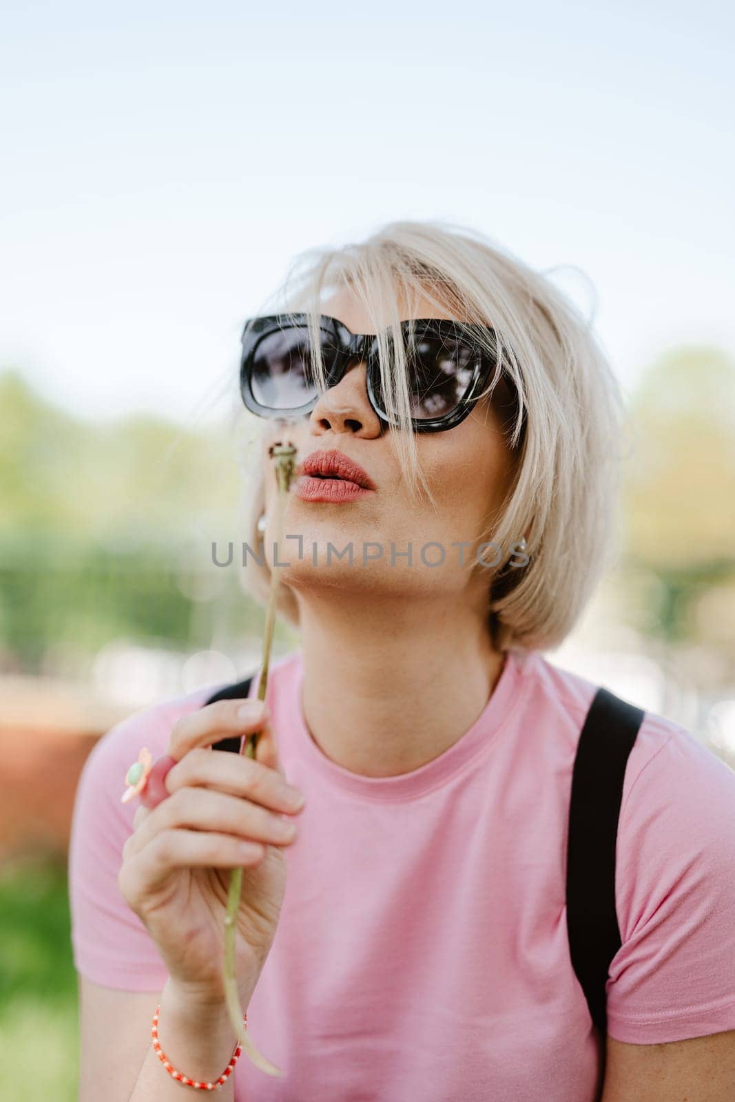 Portrait of a beautiful young woman blowing dandelion flower. Shallow dof
