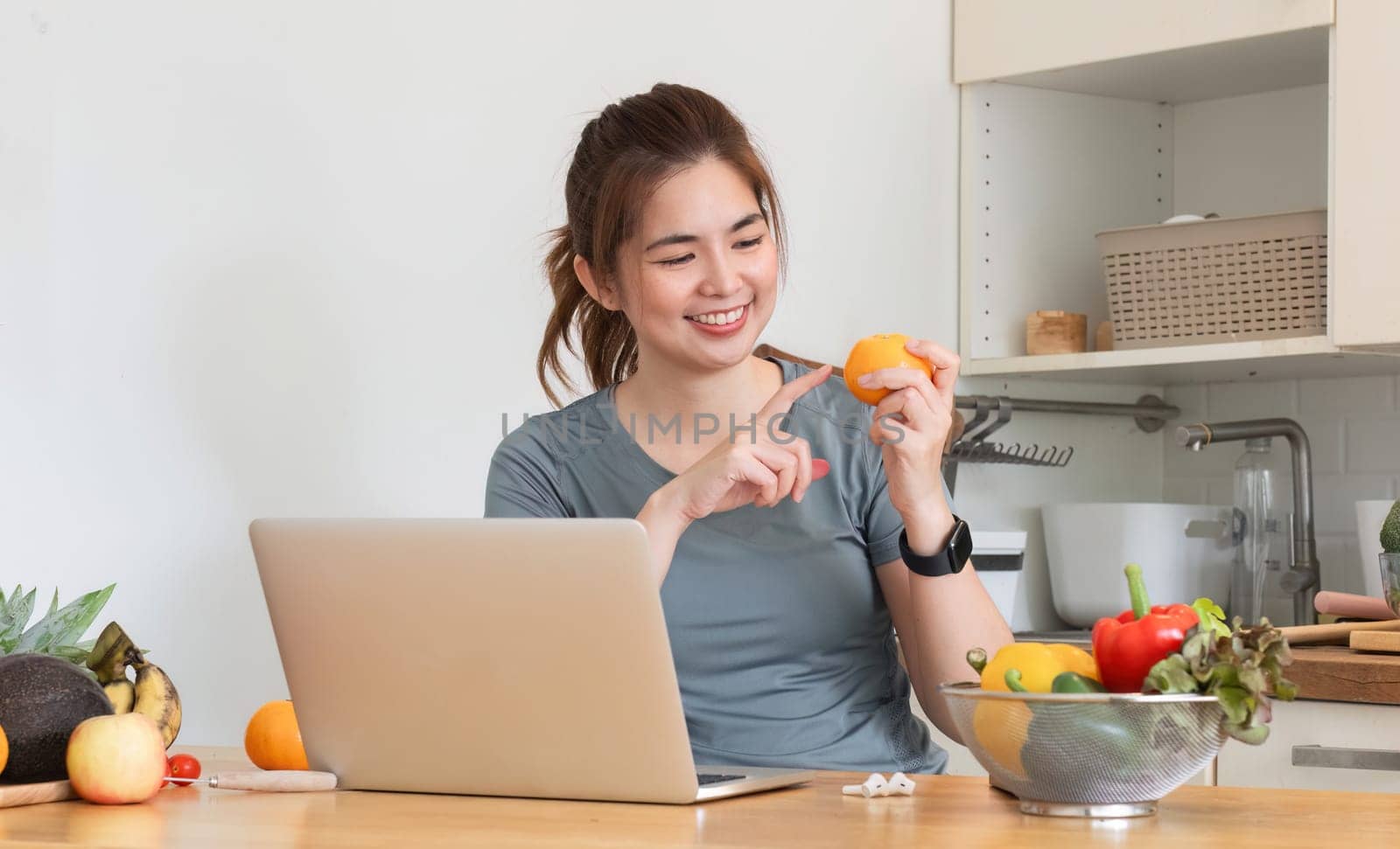 Healthy Asian woman takes care of her health by eating vegetable and fruit salad, adding vitamins in the kitchen..