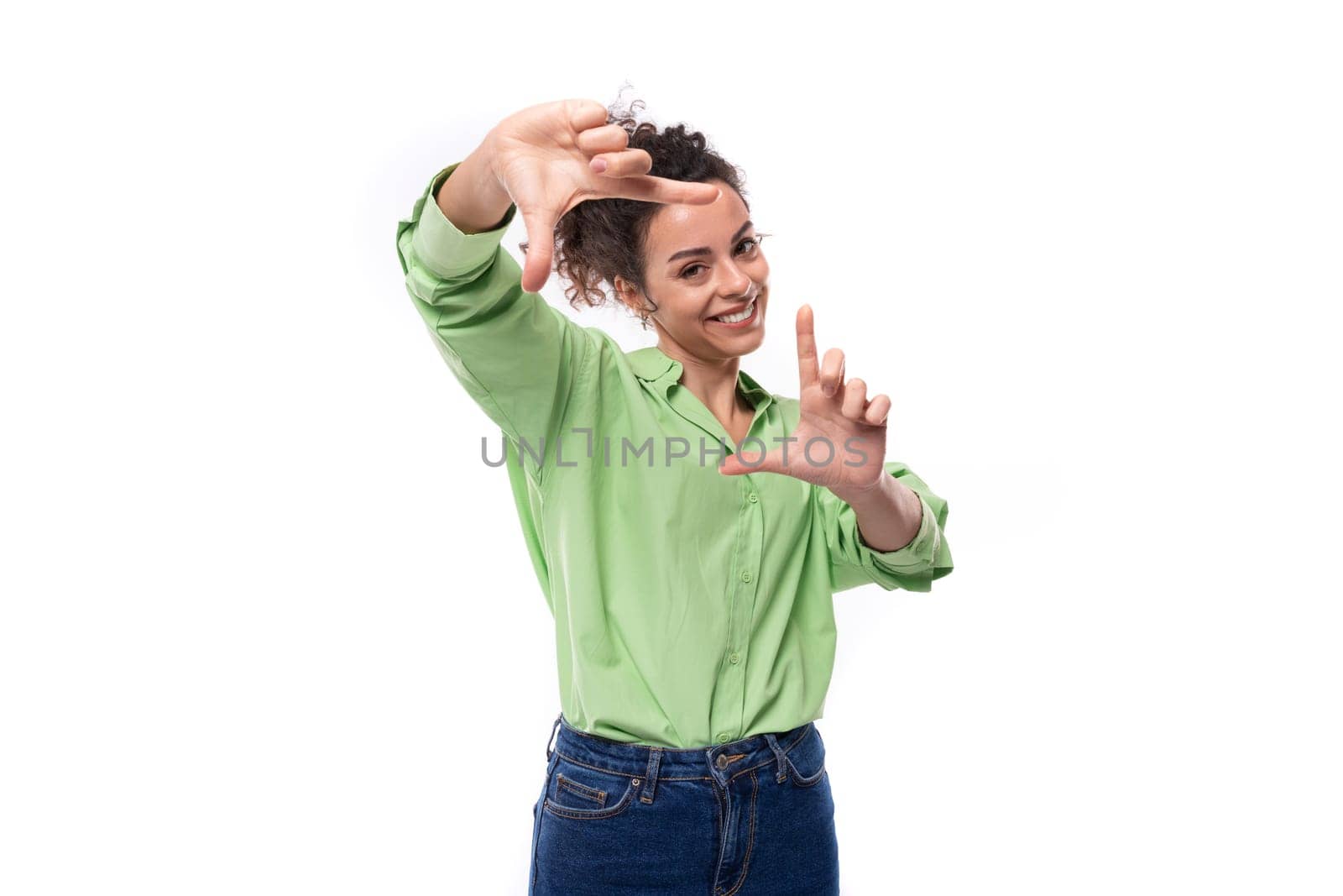 young positive brunette businesswoman with curly hair tied up in a ponytail in a light green shirt in a studio space.