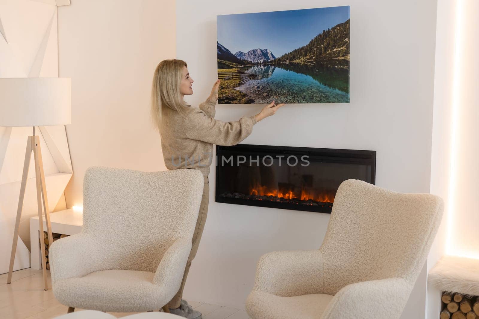 Young woman hanging a photo canvas print painting on the wall.