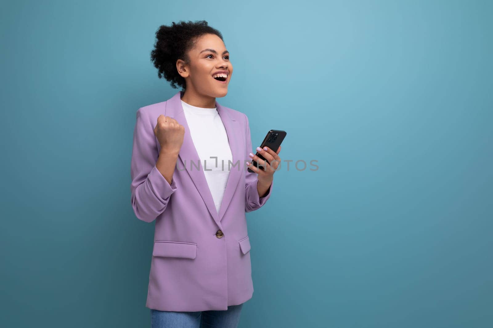 young successful hispanic brunette leader woman with curly hair rejoices holding a smartphone in her hand.