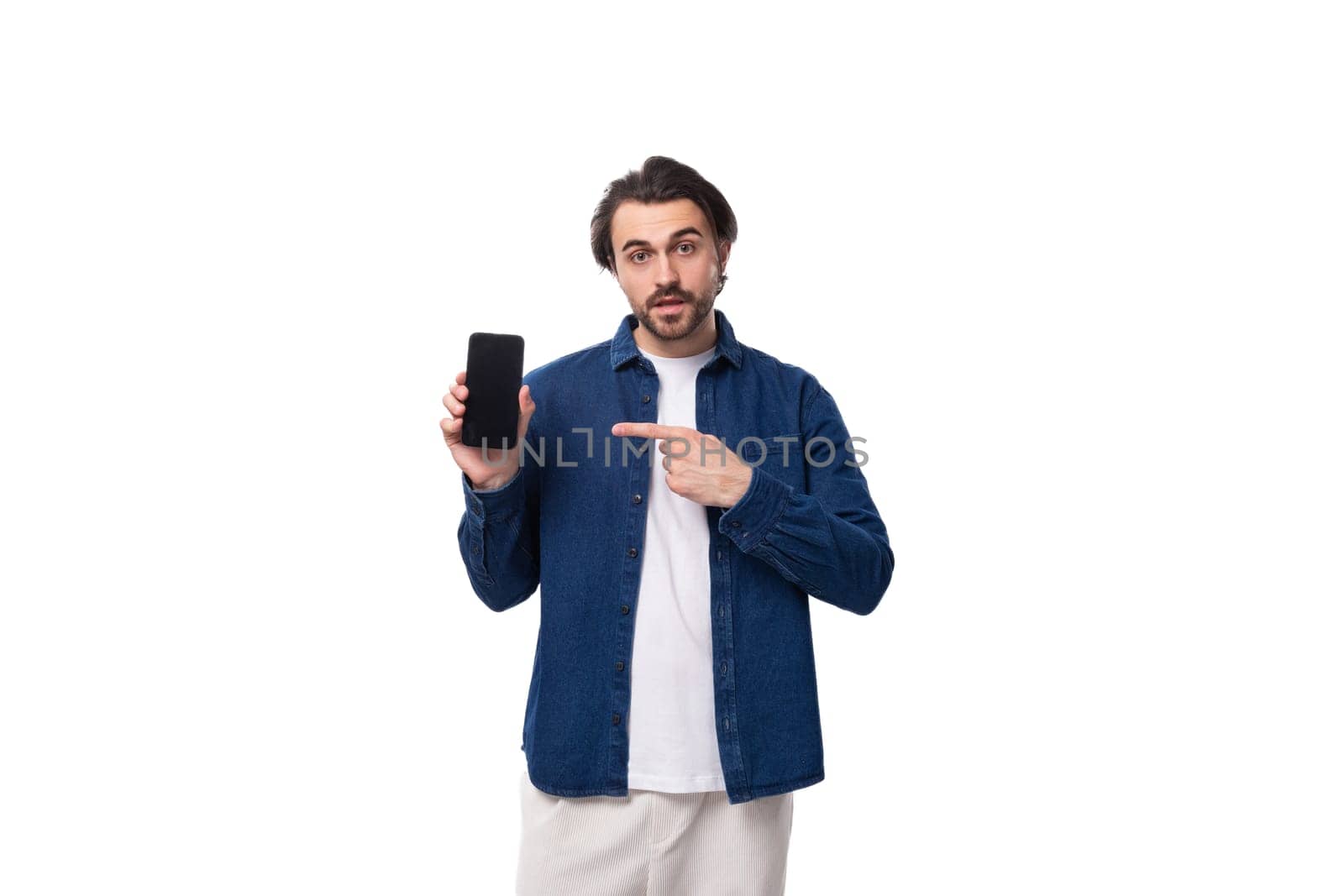 young european brutal brunette man with a cool hairstyle dressed in a denim shirt shows the screen of the phone vertically. e-business concept.