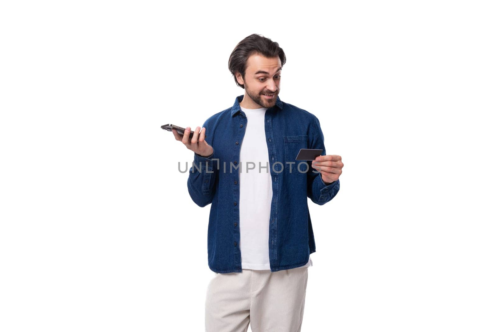 young european brunette man holding plastic credit card and smartphone with mockup. e-business advertising concept.