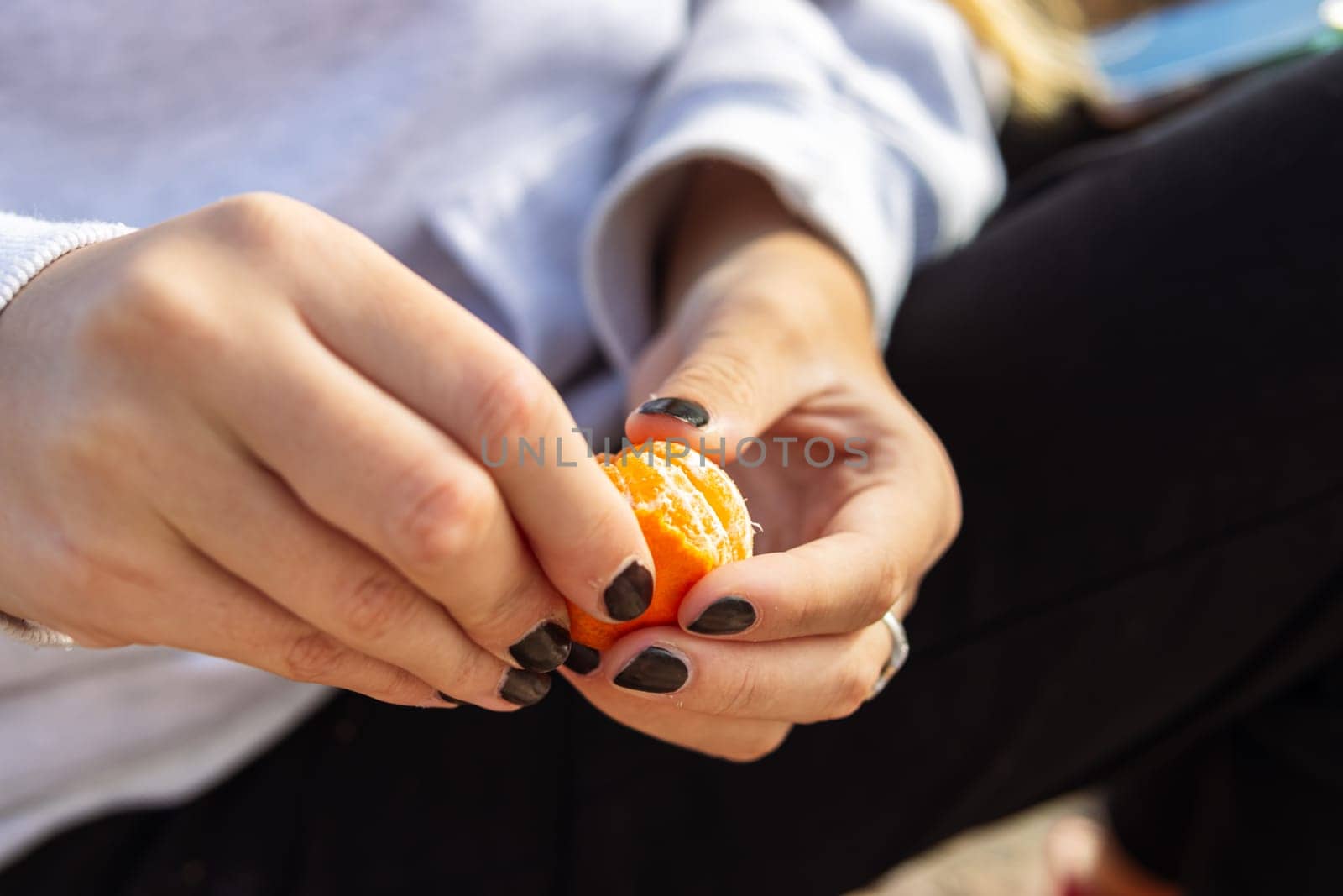 Beautiful female hands of a teenager peeling tangerines on the street with space for copy text on the right. High quality photo