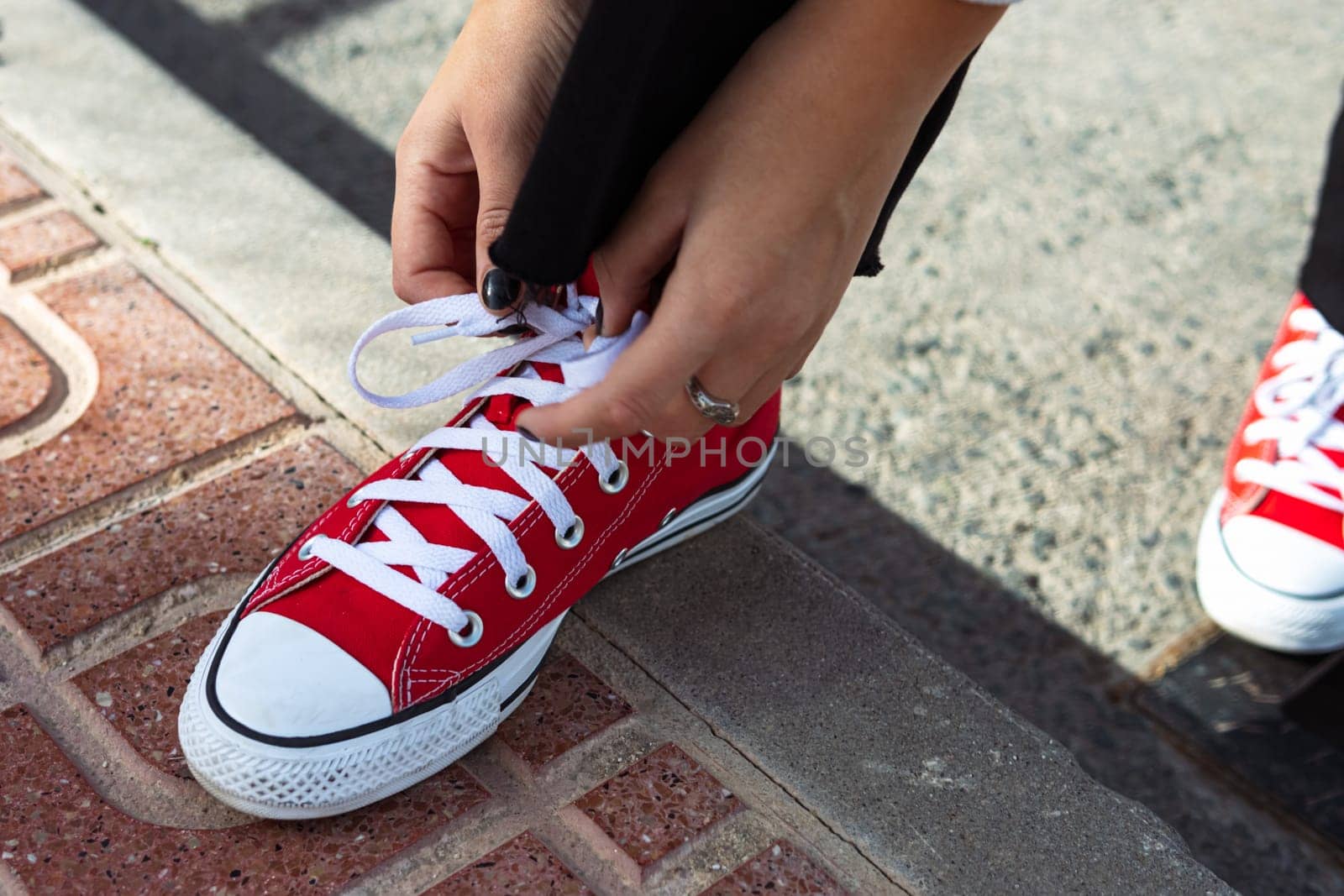 close up of the legs of a beautiful teenage girl. Young hipster woman tying laces in red sneakers by PopOff