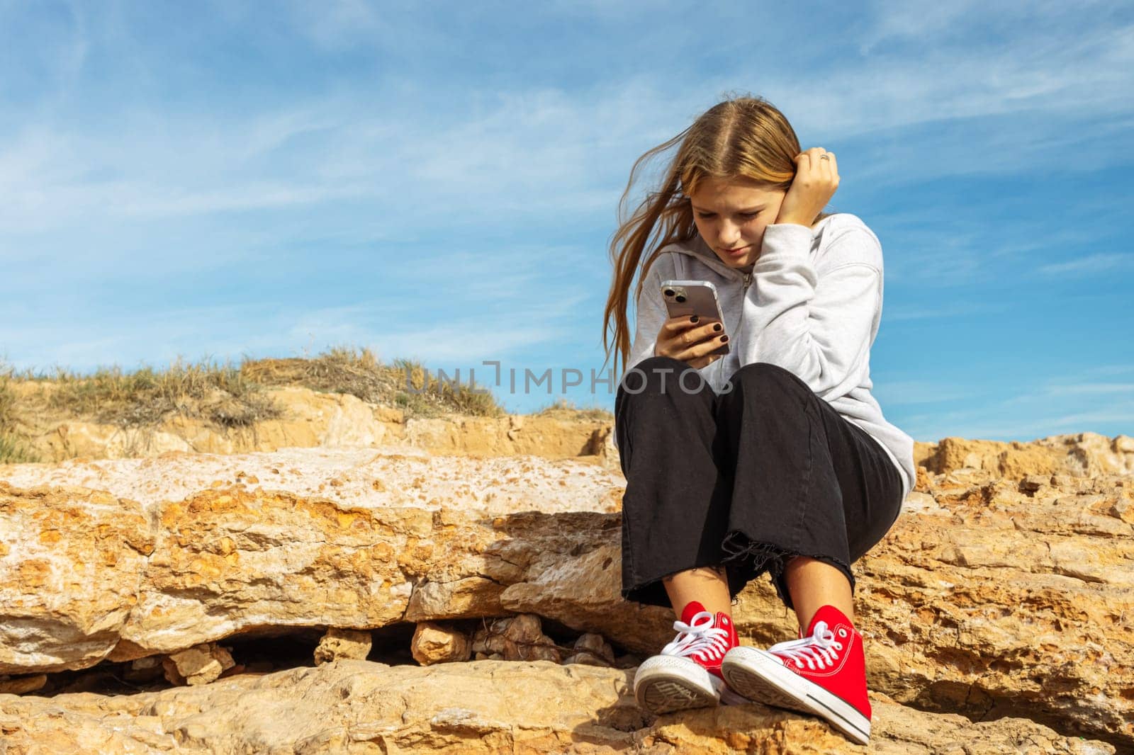 teenage girl sitting near the sea and the girl looks at the phone by PopOff