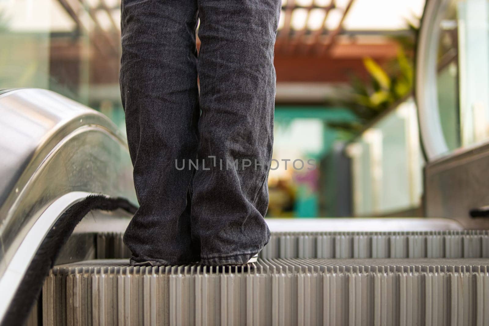 female legs stand on an escalator in a shopping center close-up by PopOff