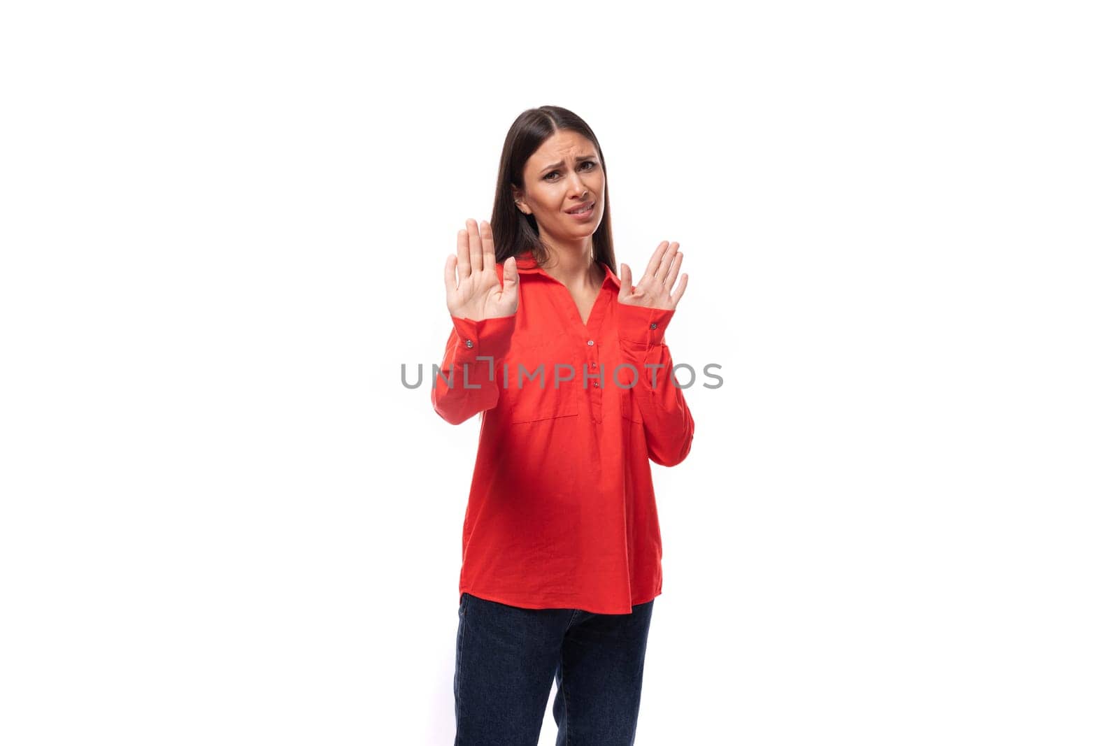 young brunette secretary woman dressed in a red shirt shows a gesture of rejection on a white background with copy space.