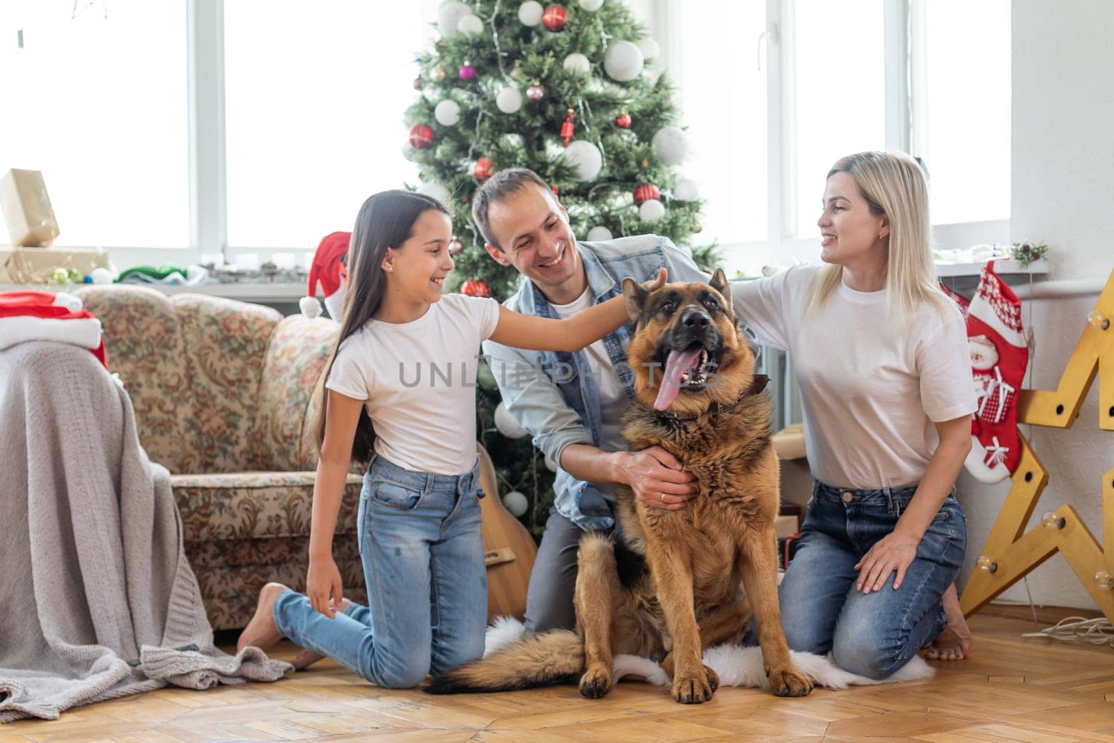 smiling family and daughter with dog sitting near christmas tree with gifts by Andelov13