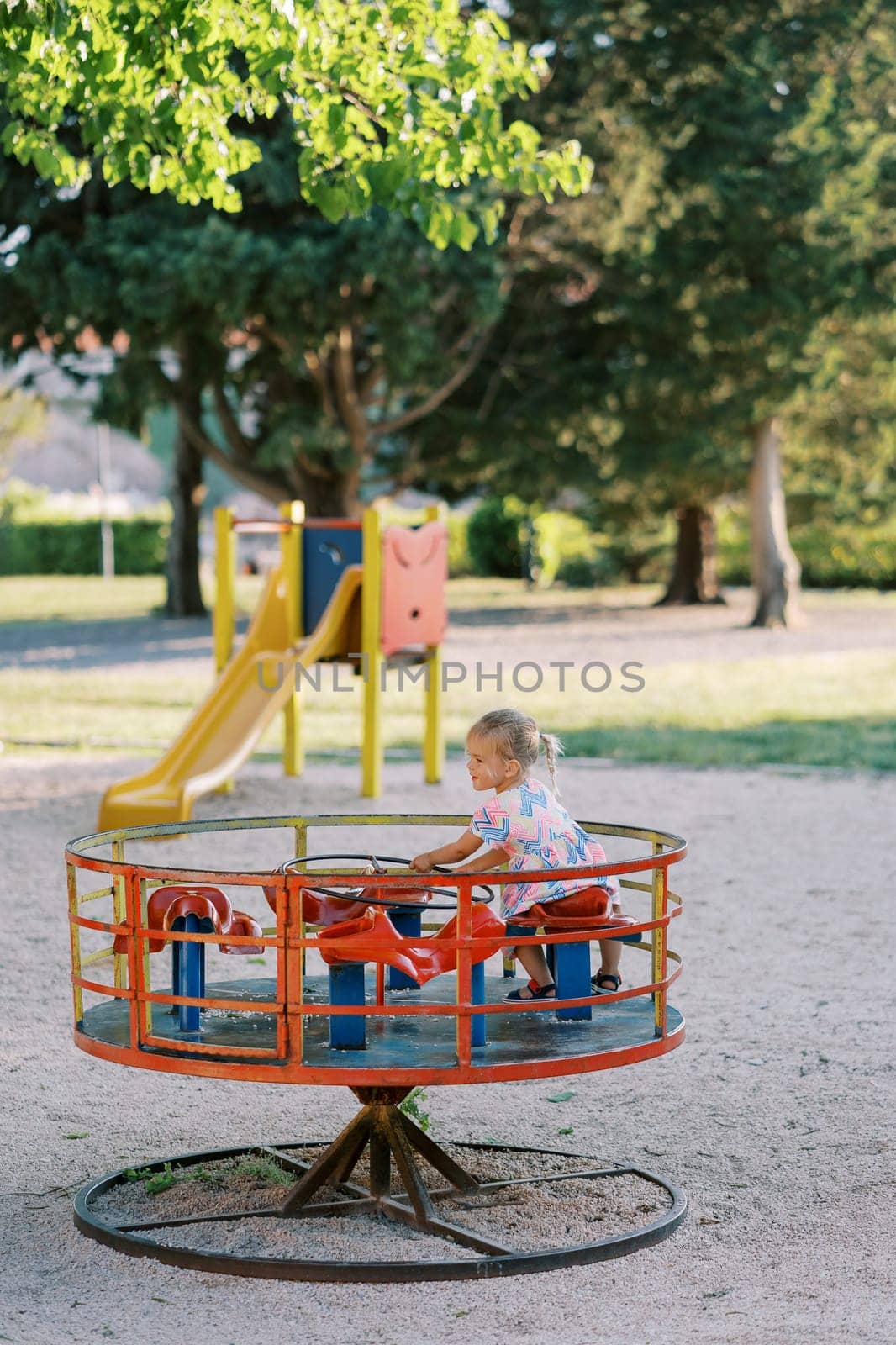 Little girl sitting on a carousel holding the steering wheel in the playground. High quality photo
