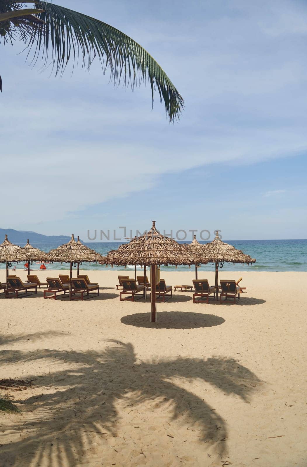 Straw sunshades and sunbeds on the empty pebble beach with sea in the background. Deserted beach with rattan sun loungers and umbrellas